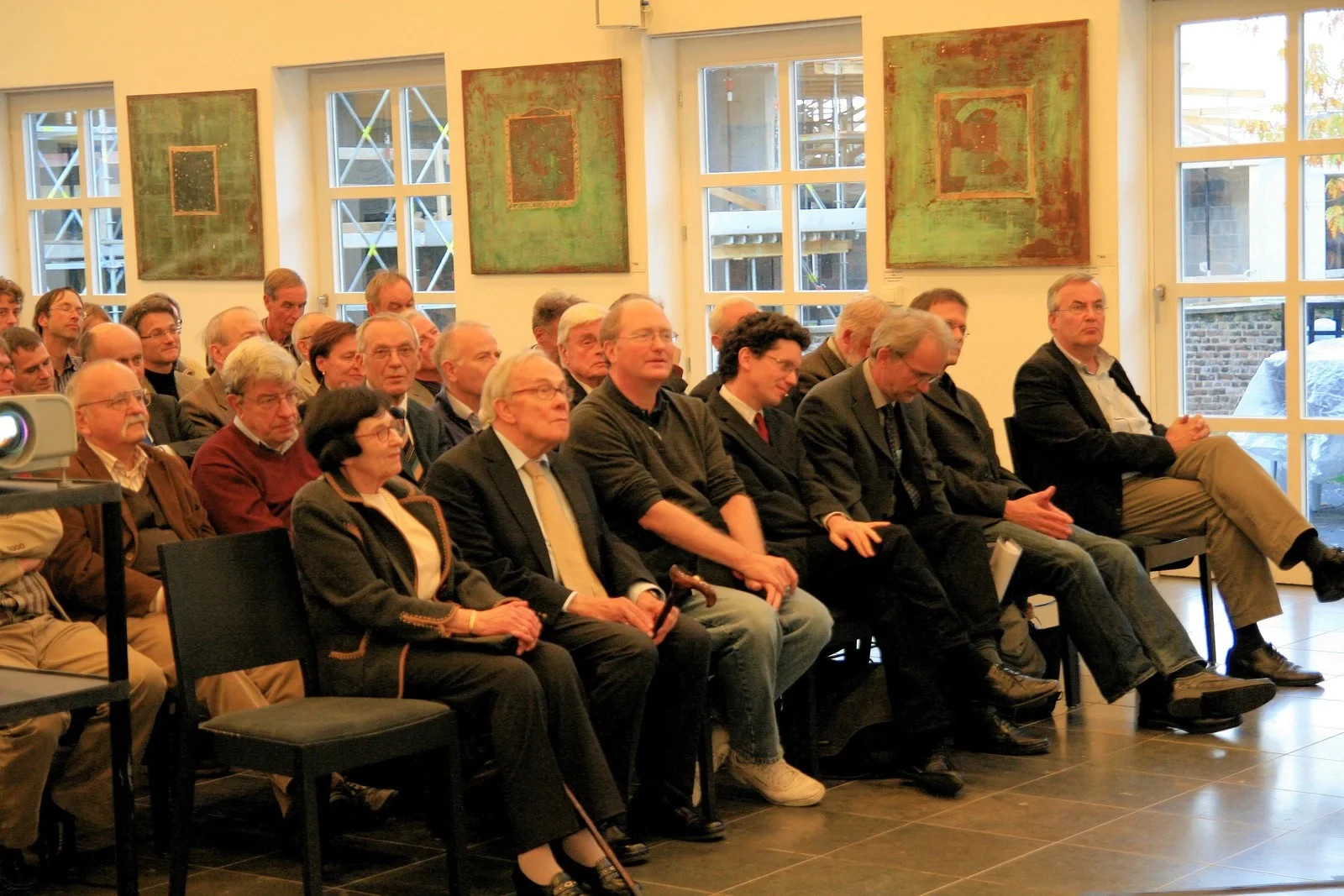 Eine Wissenschaftlerin und ein Wissenschaftler arbeiten hinter einer Glasfassade und mischen Chemikalien mit Großgeräten.
