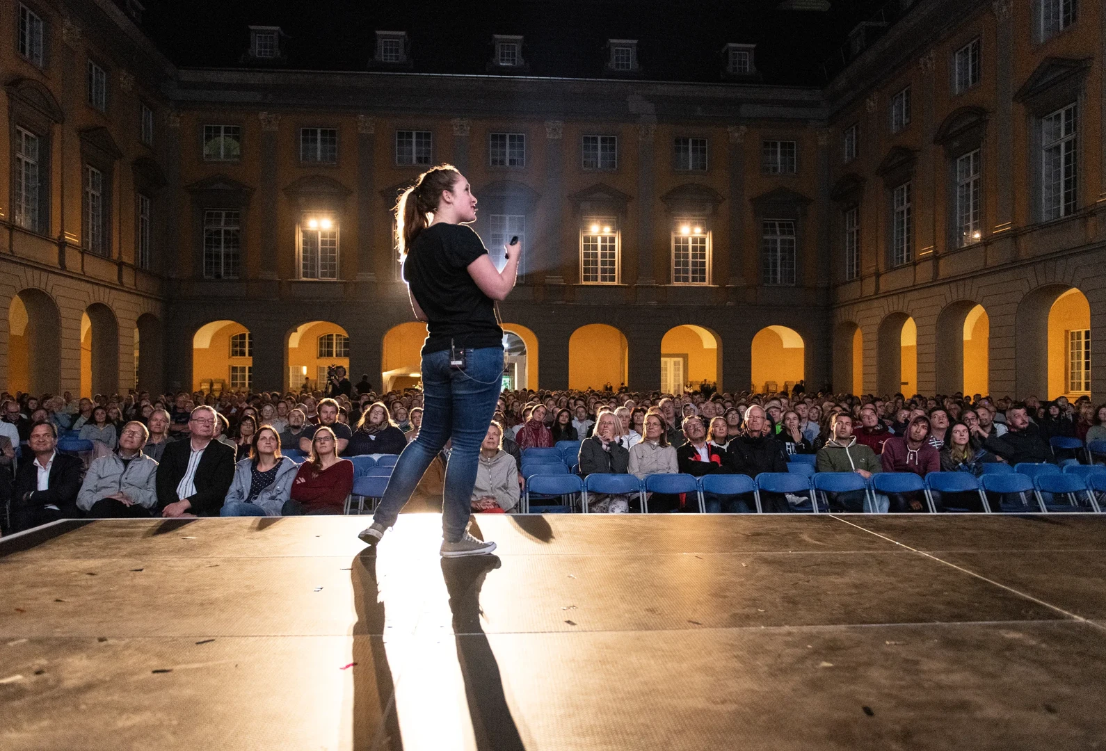 Eine Wissenschaftlerin und ein Wissenschaftler arbeiten hinter einer Glasfassade und mischen Chemikalien mit Großgeräten.