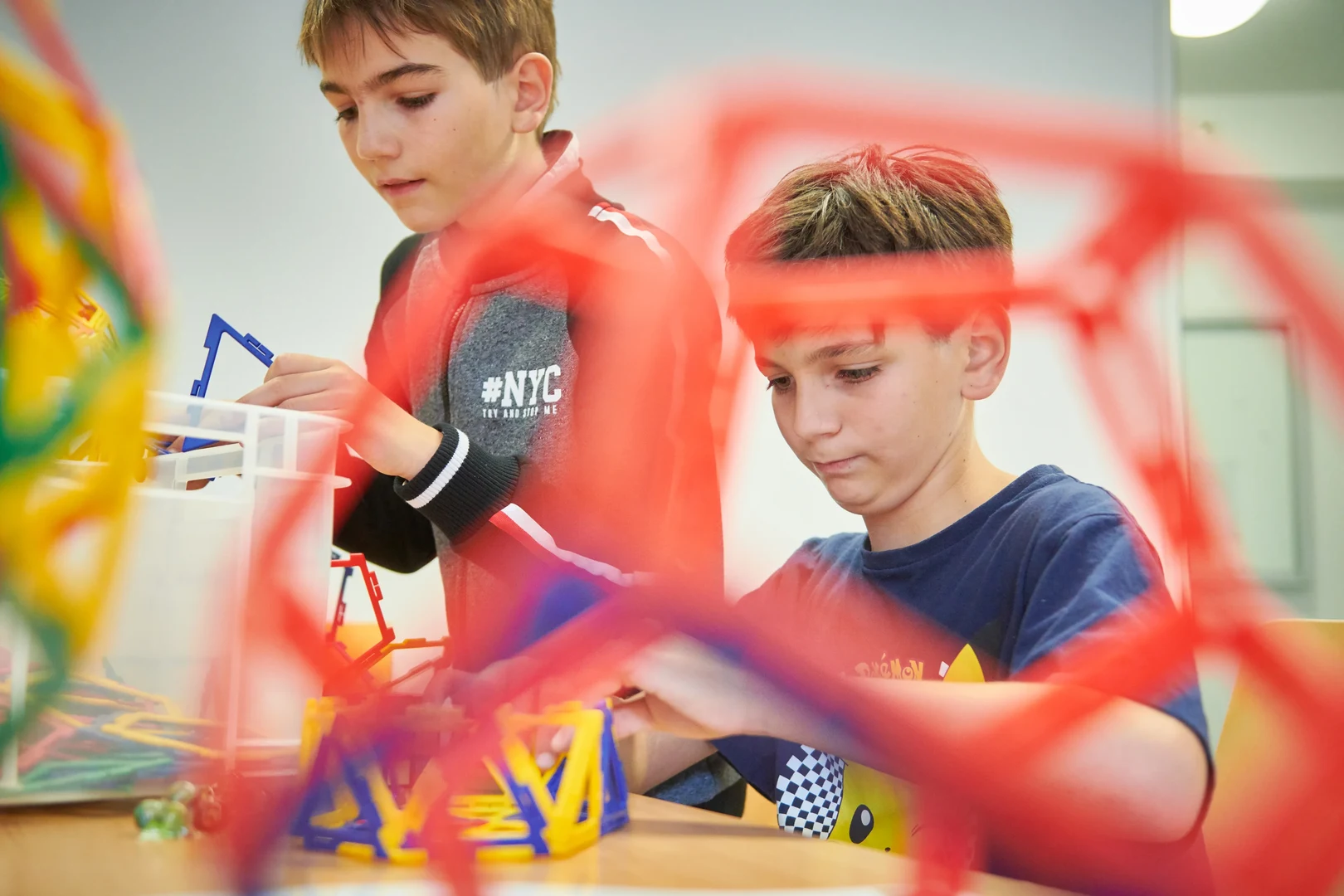 Eine Wissenschaftlerin und ein Wissenschaftler arbeiten hinter einer Glasfassade und mischen Chemikalien mit Großgeräten.